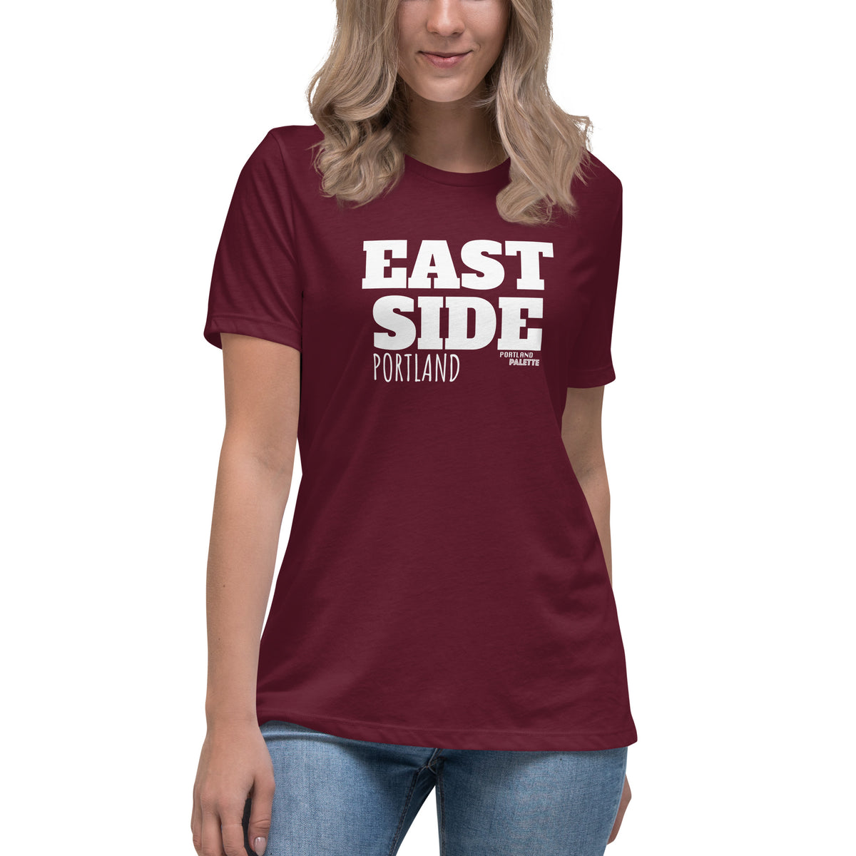 A woman wearing a maroon short-sleeve t-shirt with 'EAST SIDE PORTLAND' printed in bold white letters on the front, paired with blue jeans against a plain white background.
