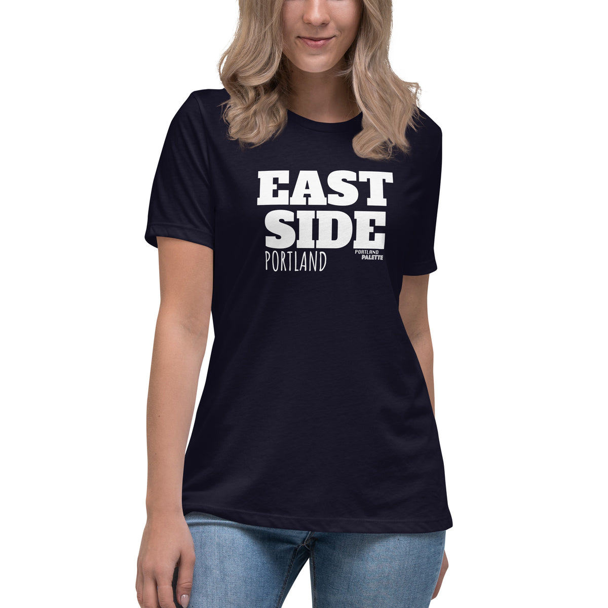 A woman wearing a navy blue short-sleeve t-shirt with 'EAST SIDE PORTLAND' printed in bold white letters on the front, paired with blue jeans against a plain white background.